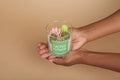 Hand holding a glass container with a cactus flower candle against a beige background