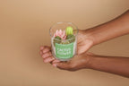 Hand holding a glass container with a cactus flower candle against a beige background