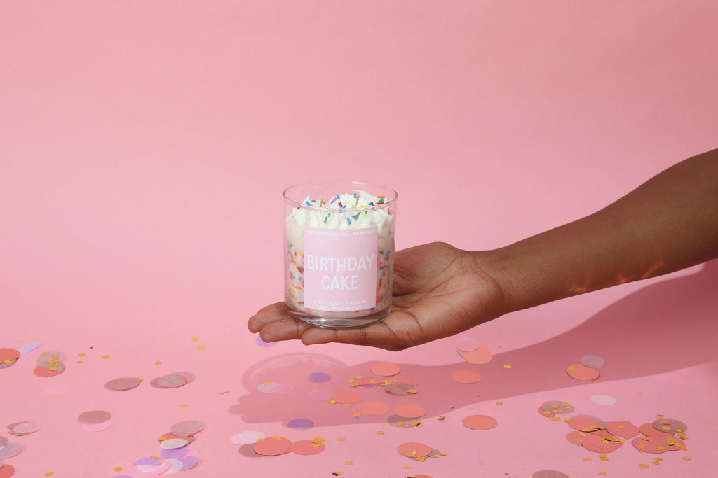 Hand holding a pink candle with sprinkles against a pink background