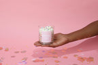 Hand holding a pink candle with sprinkles against a pink background